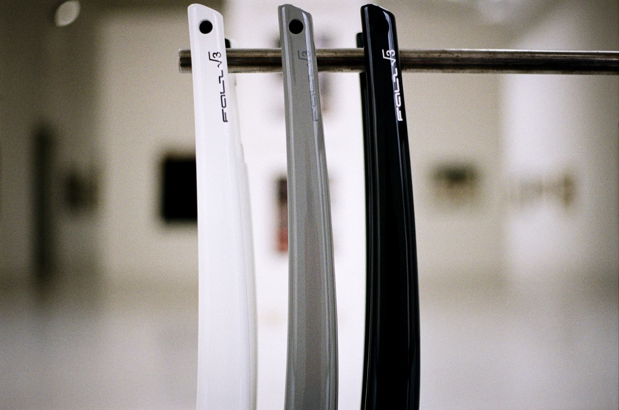 Three FOLL √3 carbon forks — white, grey and black — hanging on a rod in a gallery space