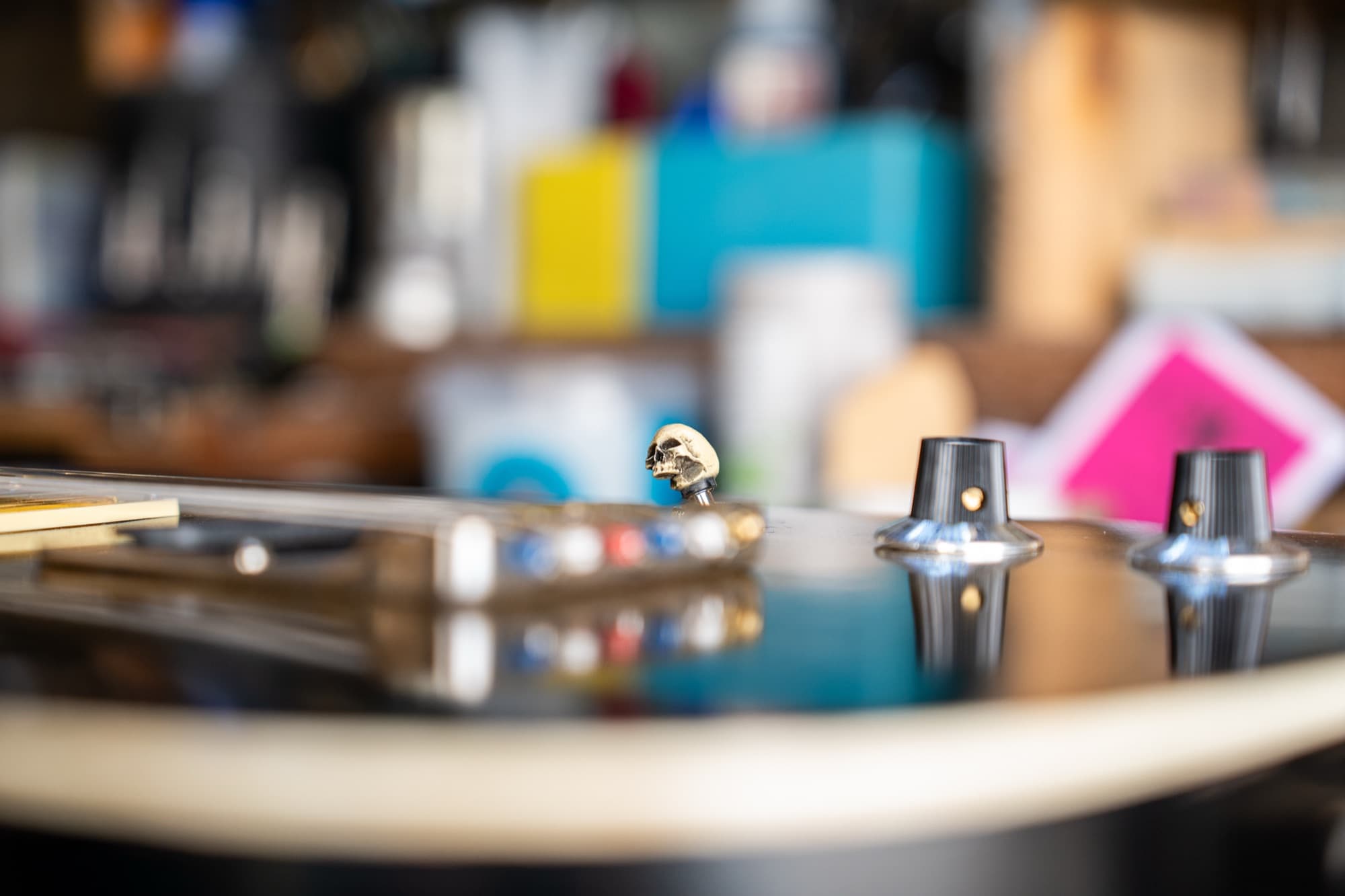 A small brass skull for a switch tip on a black guitar, the shed's shelves out of focus behind